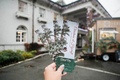 Hand holding four Christmas event tickets with greenery design.
