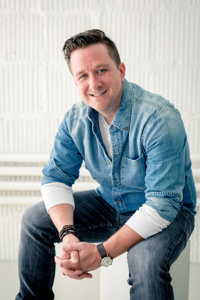 Headshot photo of man in business casual wear sitting on a stool and smiling while posing for a South Shore, MA portrait photographer