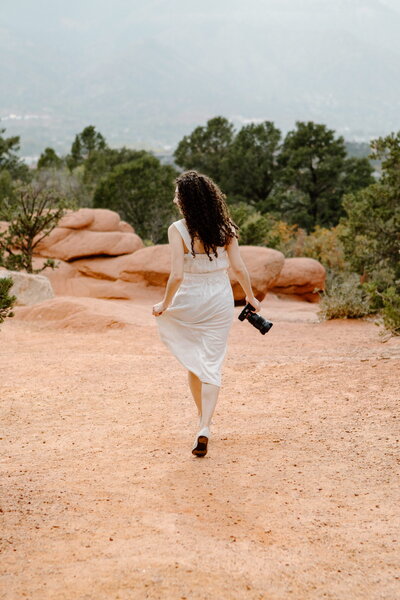 girl in dress holding camera and running away