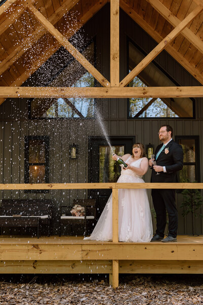 Couple popping champagne at their a-frame airbnb.