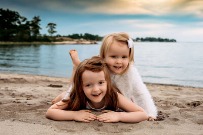Sisters laying with each other on a beach in Stamford, CT for their family session.