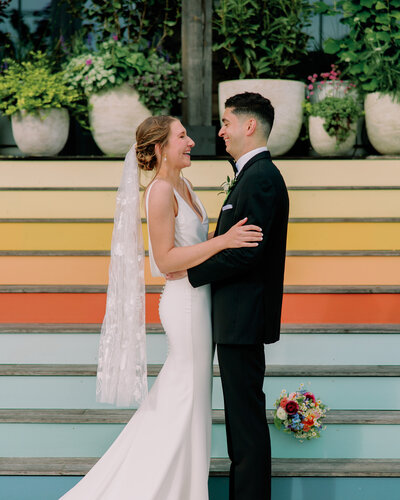 A wedding couple laughing as they have their arms wrapped around each other 
