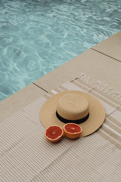 A holiday vibe sunhat with ripe citrus fruit at the edge of a blue swimming pool in summer, symbolising Financial Freedom and Abundance.