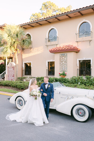 Bride and groom walking in front of a vintage car at their wedding