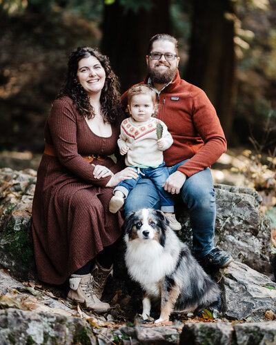Vancouver WA Wedding Photographers Lindsey and Hunter Wickert sitting on a rock in a forest with their toddler and dog