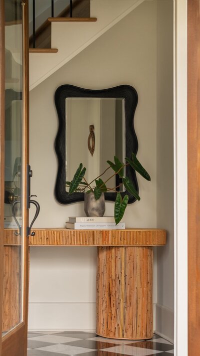 Modern eclectic Raleigh foyer with fluted wood entry table, sculptural black mirror, statement books, and plant styling in warm tones.