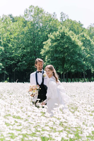 bride and groom in a daisy field at Château de champlâtreux holding a bouquet and looking at the camera taken by a  Wedding Photographer in Dallas