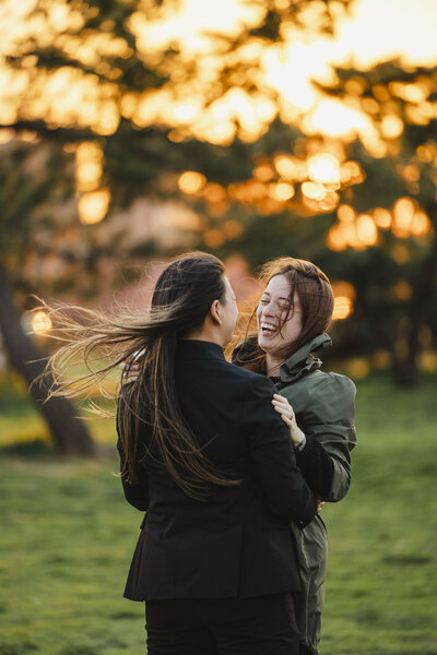 A couple with their arms around each other laughing together in a field 