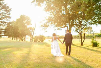 Bride and groom holding hands walking toward the sun, taken by photographers minneapolis