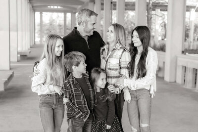 family of 6 standing posed together and looking at eachother and smiling in black and white