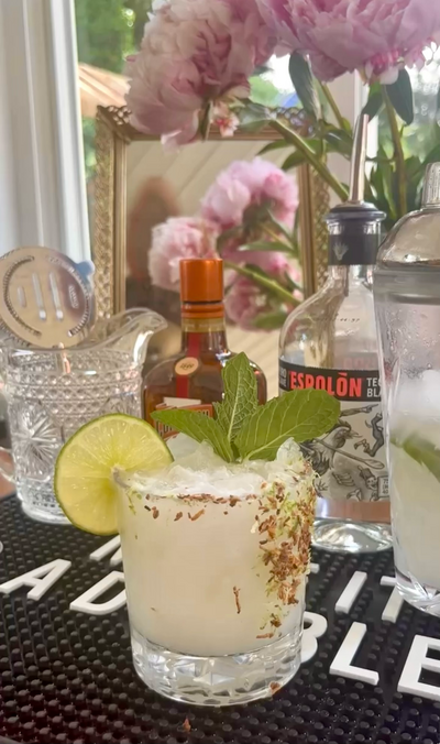 cocktail with fresh herbs lime wheel and toasted coconut flakes in a margarita glass