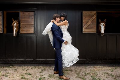 Groom picking up bride in an embrace in horse stables