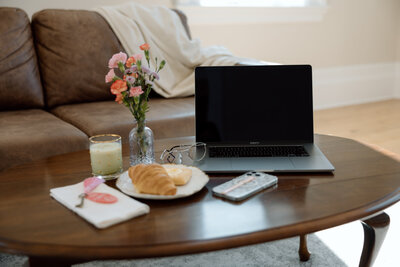 Cozy setup with laptop, coffee, croissant, and flowers on a coffee table—illustrating ready-to-use templates trusted by over 200 social media managers to save time and reduce stress.
