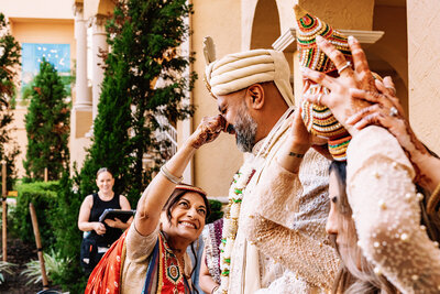 A woman performing a traditional gesture by placing a decorative item on the groom’s nose during an Indian wedding ceremony. Captured by Shannon, an Orlando, Florida Indian Wedding Photographer.