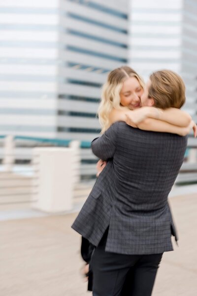 Couple laugh while woman has arms wrapped around man's neck. during engagement photoshoot.