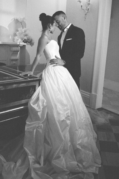 elegant bride and groom hold hands and gaze at each other lovingly, black and white