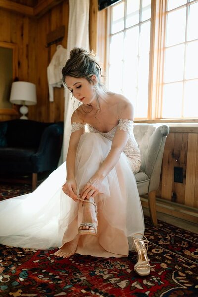 The bride elegantly fastens her wedding shoe while seated on a sturdy chair
