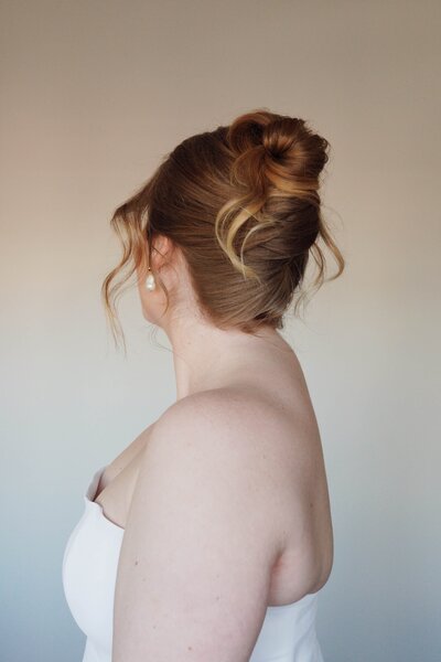 Bride with a soft, romantic high bun and delicate curls — whimsical wedding hairstyle by Klover Beauty’s Maryland team.