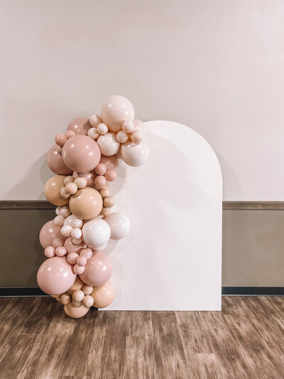 Creamy neutral balloon garland attached to a white arch backdrop