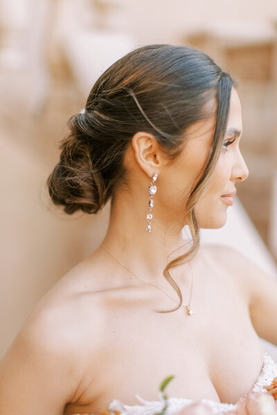 A bride smiles in the light as a brides maid helpers her get ready.