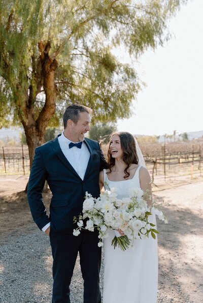 Father and Bride with bouquet standing together outside smiling and laughing