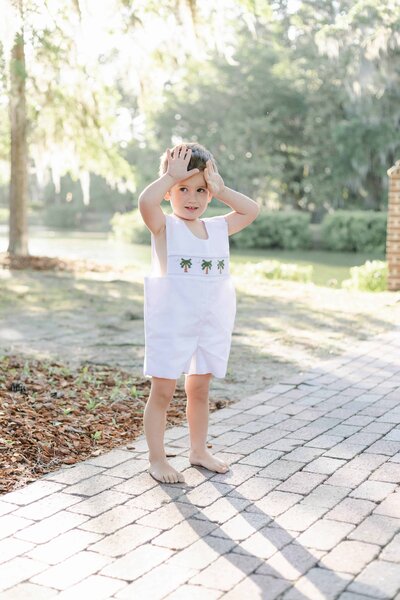 A small child standing on a brick path in Palmetto Bluff, South Carolina with his hands on his head wearing a Peter Pan collared jumper, captured by Hilton Head Photographers.