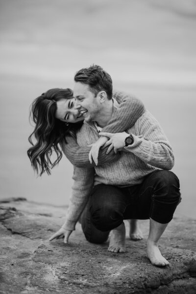 Couple  crouching on a rock with the girl hugging the guy from behind and laughing