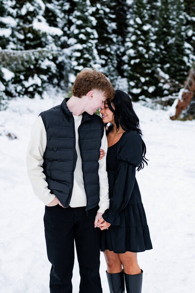 Winter engagement session in the snow and the woman is holding hands with the man