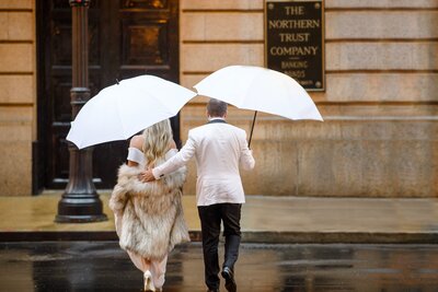 High end wedding portrait of a couple walking across a road holding white umbrellas