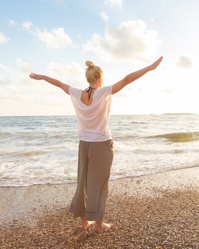 Woman standing by the sea, arms open wide, symbolizing freedom and empowerment during menopause.