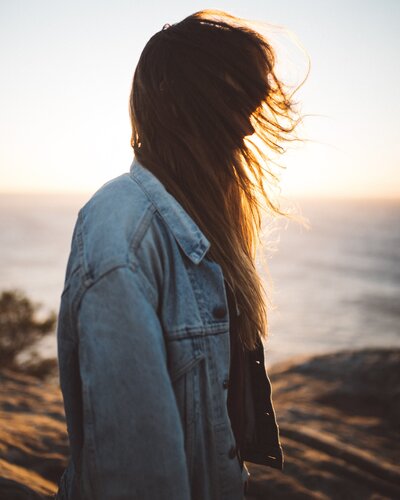 Woman in jean jacket blocking the evening sun with her long, flowing hair
