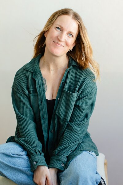 a woman with strawberry blonde hair smiles pleasantly at the camera in a green cardigan