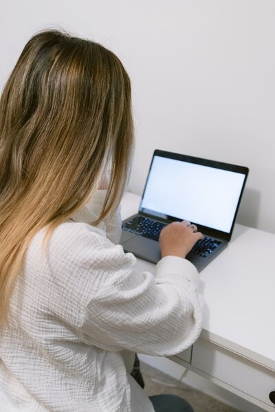 Brunette female typing on a laptop at a white desk