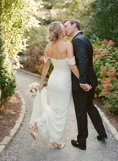 Bride and groom kissing as they walk through a blooming garden at their wedding in New England