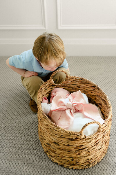 Big brother looks down at his newborn sister as she sleeps in a basket below