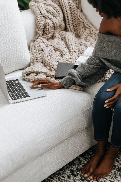 black lady on sitting on couch with laptop