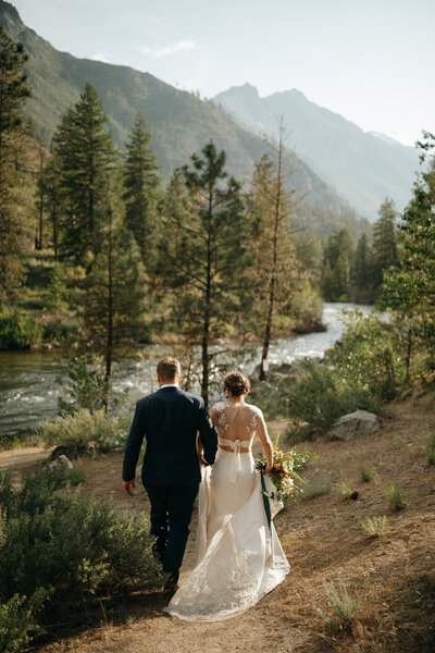 Bride and groom walking by river in mountains
