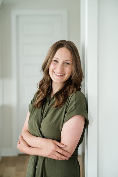 Columbus headshots of woman in a green blouse crossing her arms and smiling as she leans back on a door frame