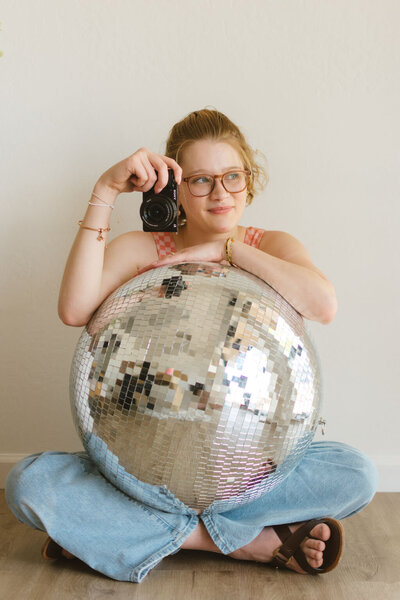 Playful branding portrait of Lillian sitting on the floor with a disco ball, representing creative virtual assistant services.