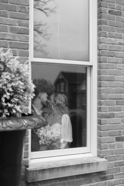 Bride and groom photographed through the window from outside their Cincinnati wedding venue, capturing an intimate and romantic moment indoors.