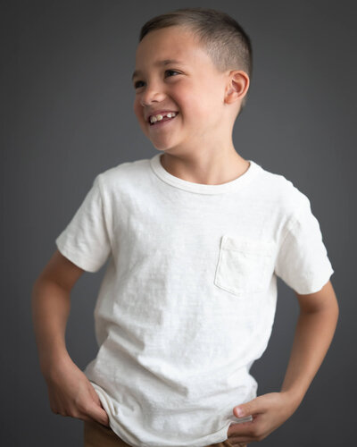 little boy in white shirt against dark backdrop looking away smiling
