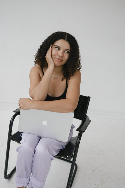 Photo of Catryce looking to her right while sitting in a chair with a laptop in her lap