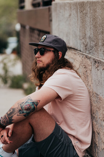 man with tattoos sat against a wall