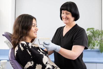 Dental assistant holding up teeth shades next to smiling patient in chair