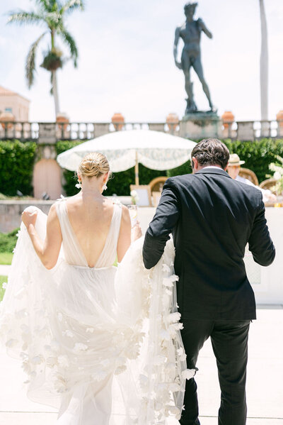 Bride and groom walk hand in hand at their elegant wedding at The Ringling Museum in Sarasota, Florida. A luxurious, European-inspired wedding celebration.