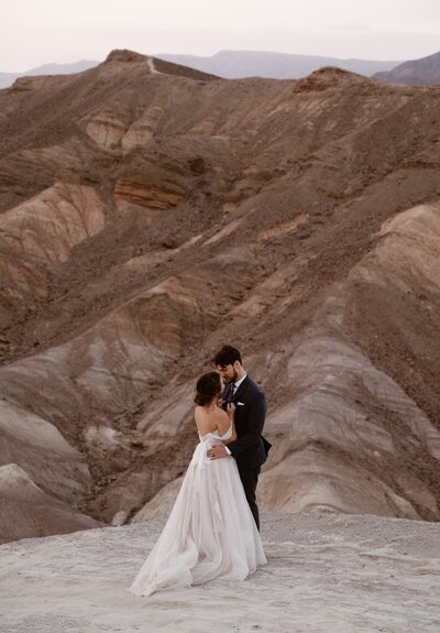 Couple in wedding attire kissing with brown canyon in the background.