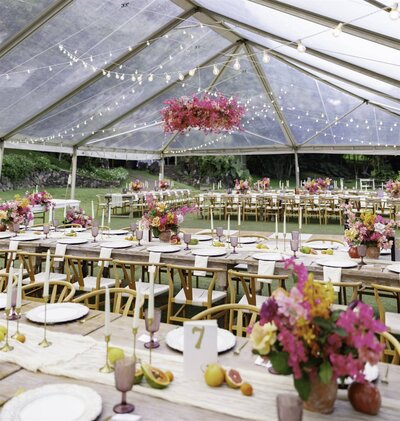 A wedding reception venue under a tent with colorful flowers and long tables 