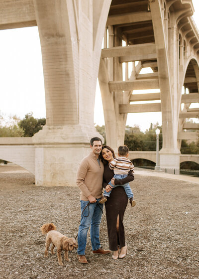 Family with their dog smiling under the Colorado street bridge during a fall family session at Desiderio Park in Pasadena, CA