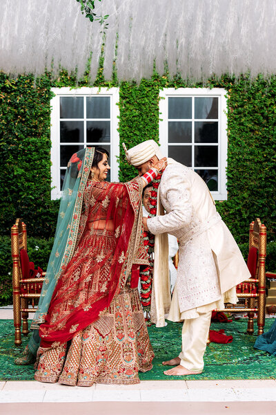 Shannon Lee, an Orlando wedding photographer capturing a beautiful cultural moment as a couple exchanges garlands during their wedding ceremony, surrounded by vibrant decor and lush greenery.