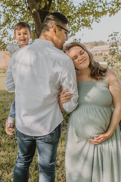 Couple posing with their toddler son while mom is holding her pregnant belly as they are excited to welcome baby brother into the family